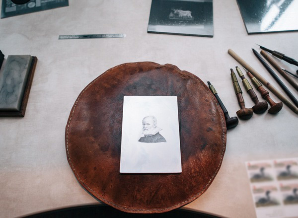 Table with old fashioned etching tools and leather disk with a picture of historical figure on it